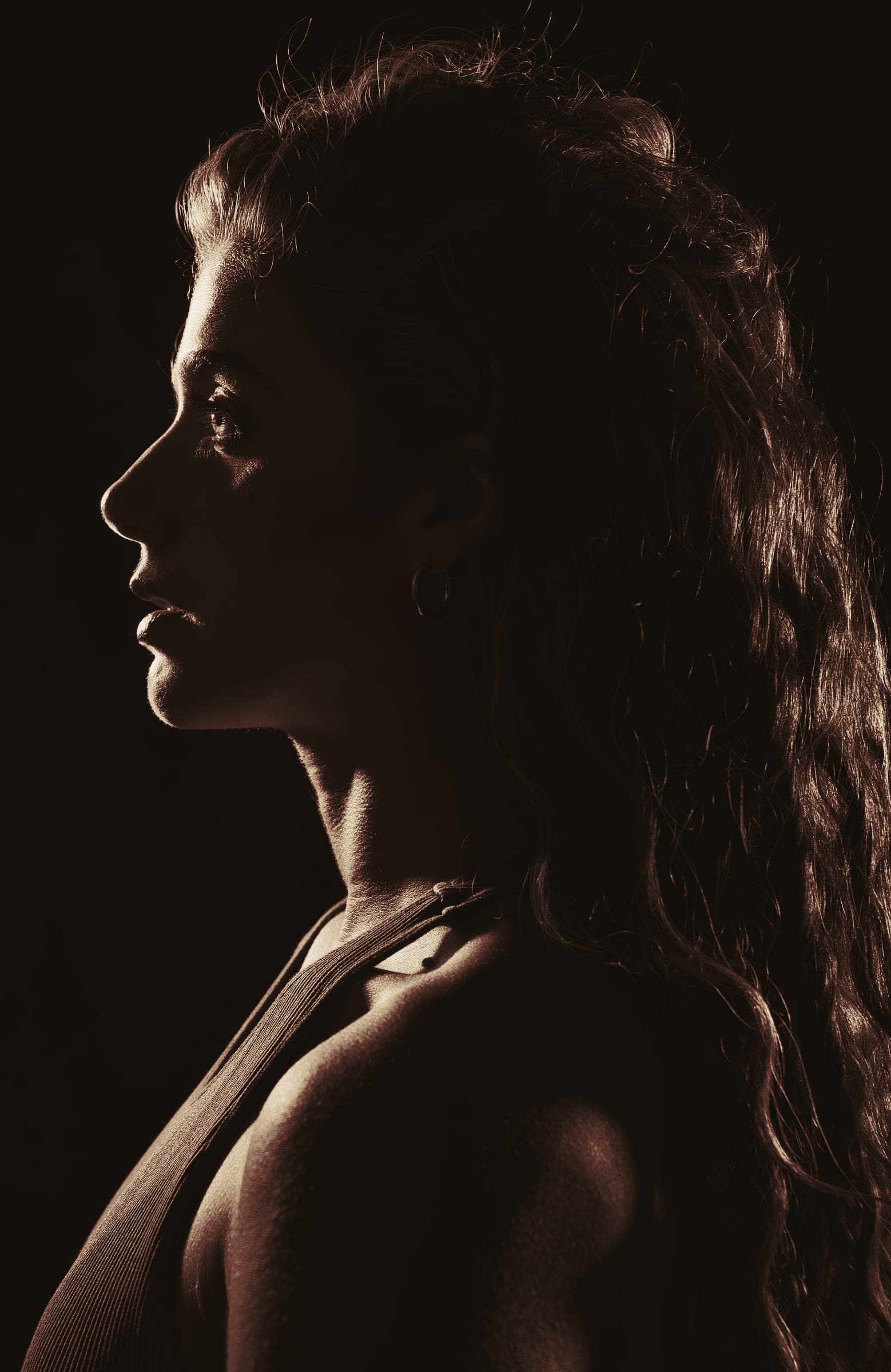 A woman in profile against a dark background, light catching the edges of her long hair.