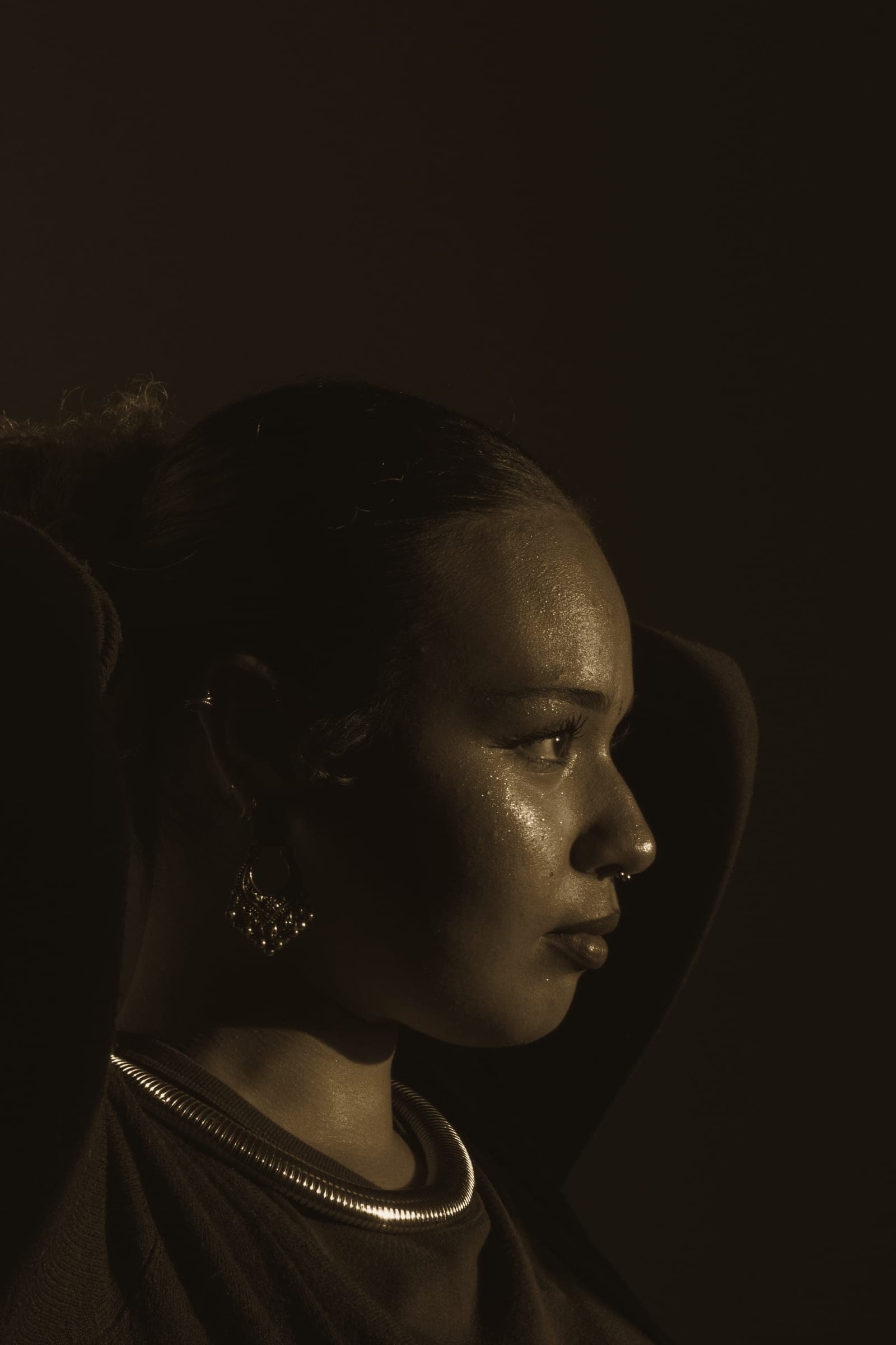 A woman in three-quarter profile, lit by soft warm light, looking away from the camera.