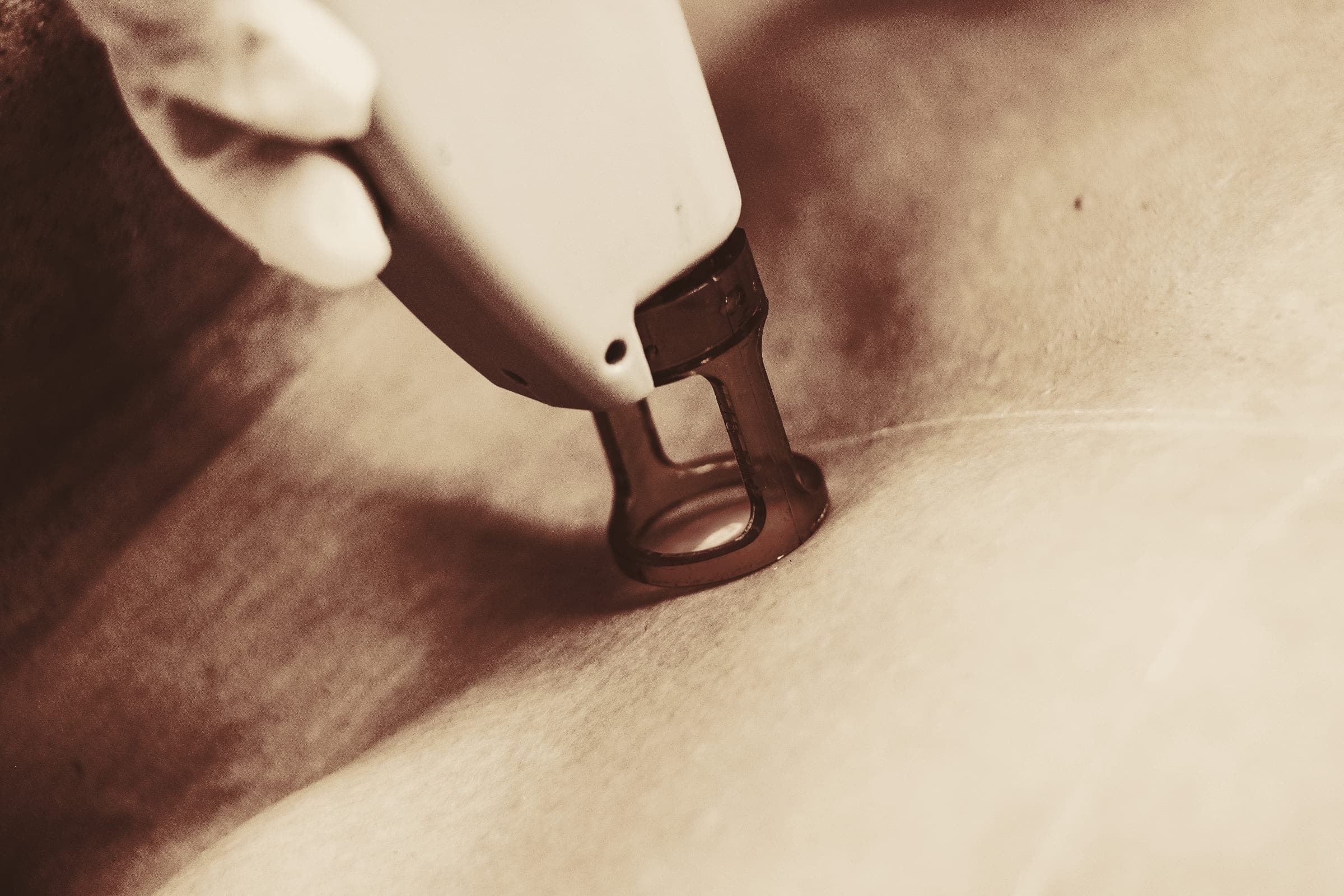 A gloved hand holding a light-based device handpiece against skin, in warm light.