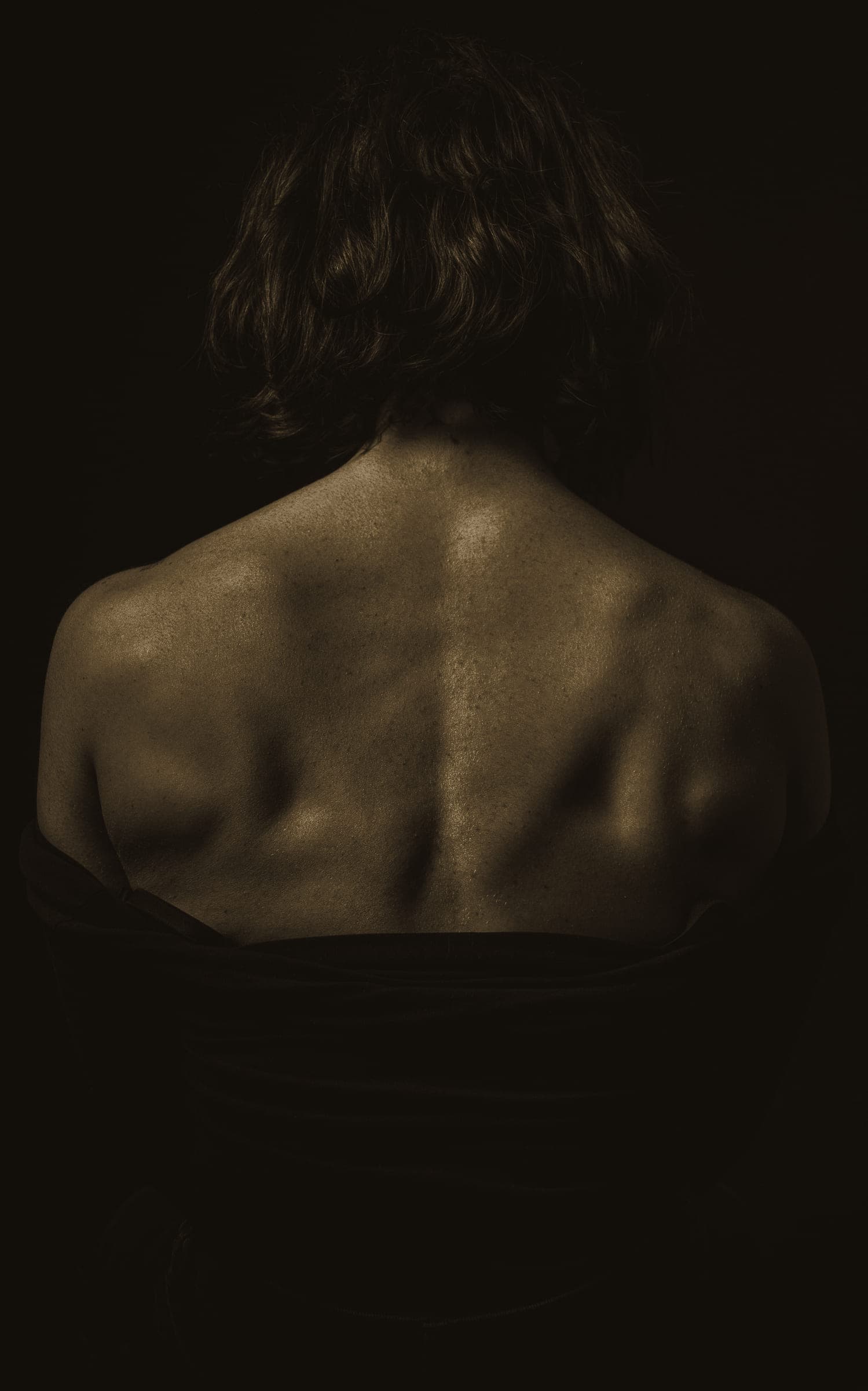 A bare back and shoulder blades in black-and-white, emerging from shadow.