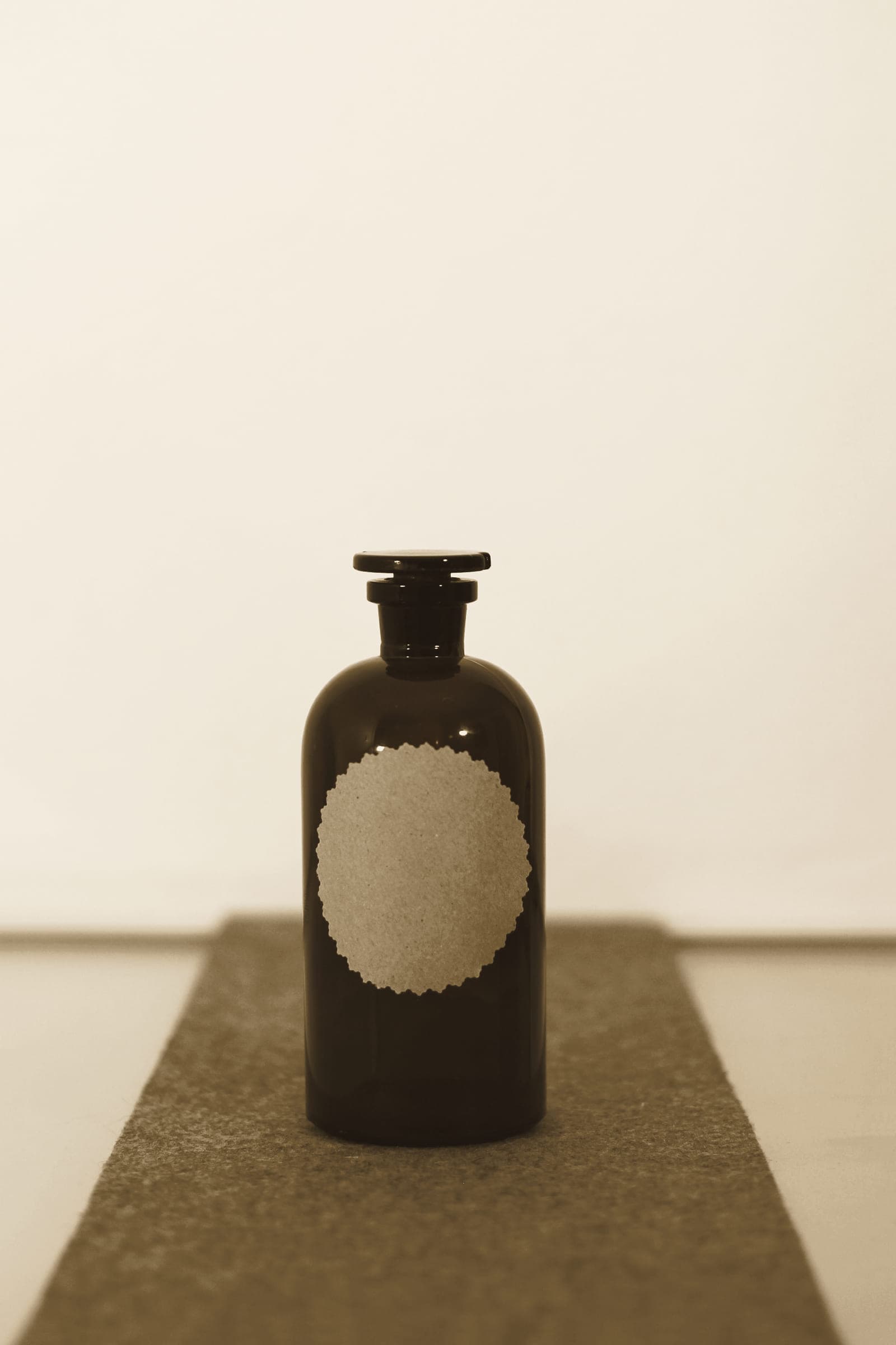 A single amber apothecary bottle on a grey stone plinth against a pale wall.