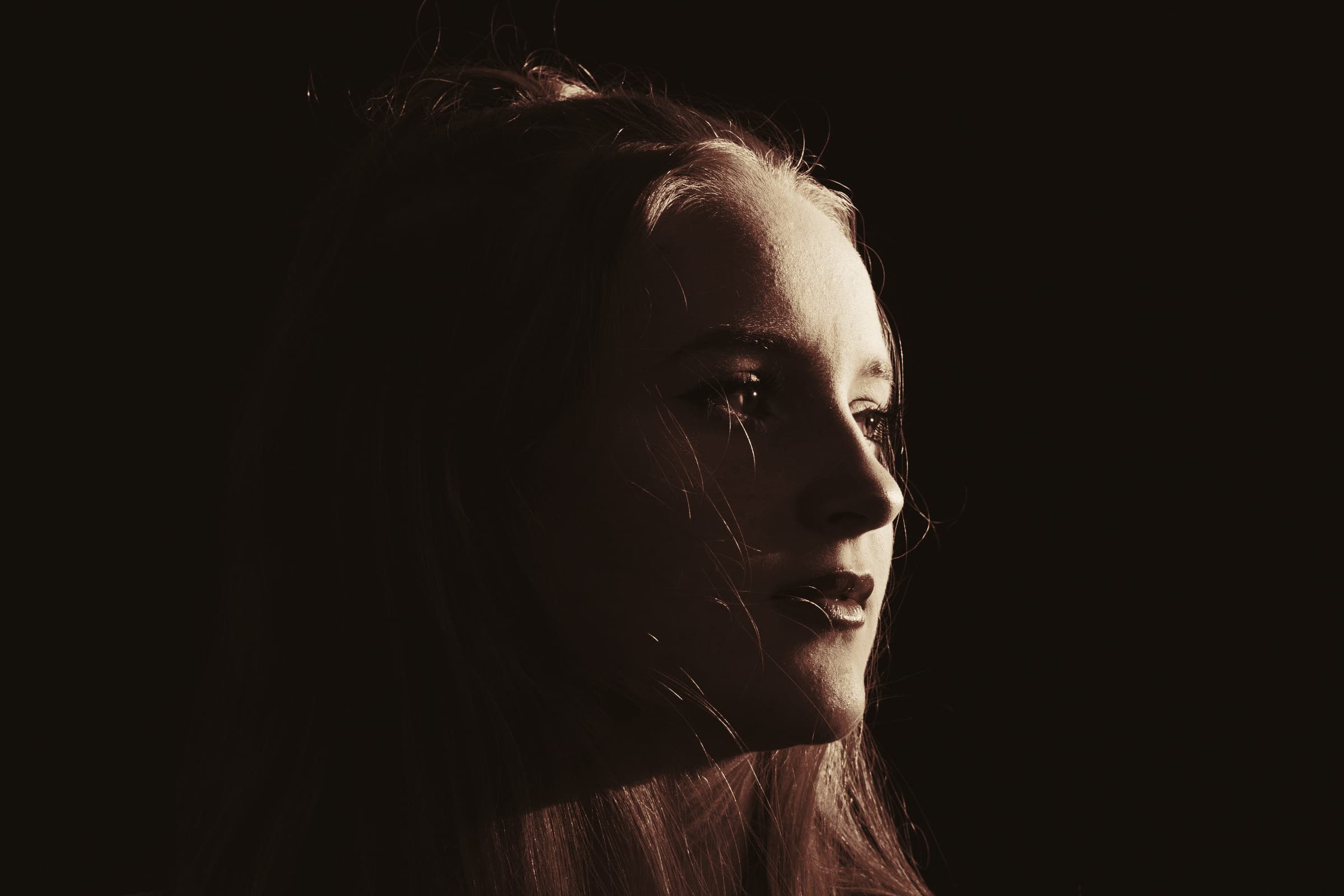 A woman in three-quarter profile in a dark room, light catching her hair.