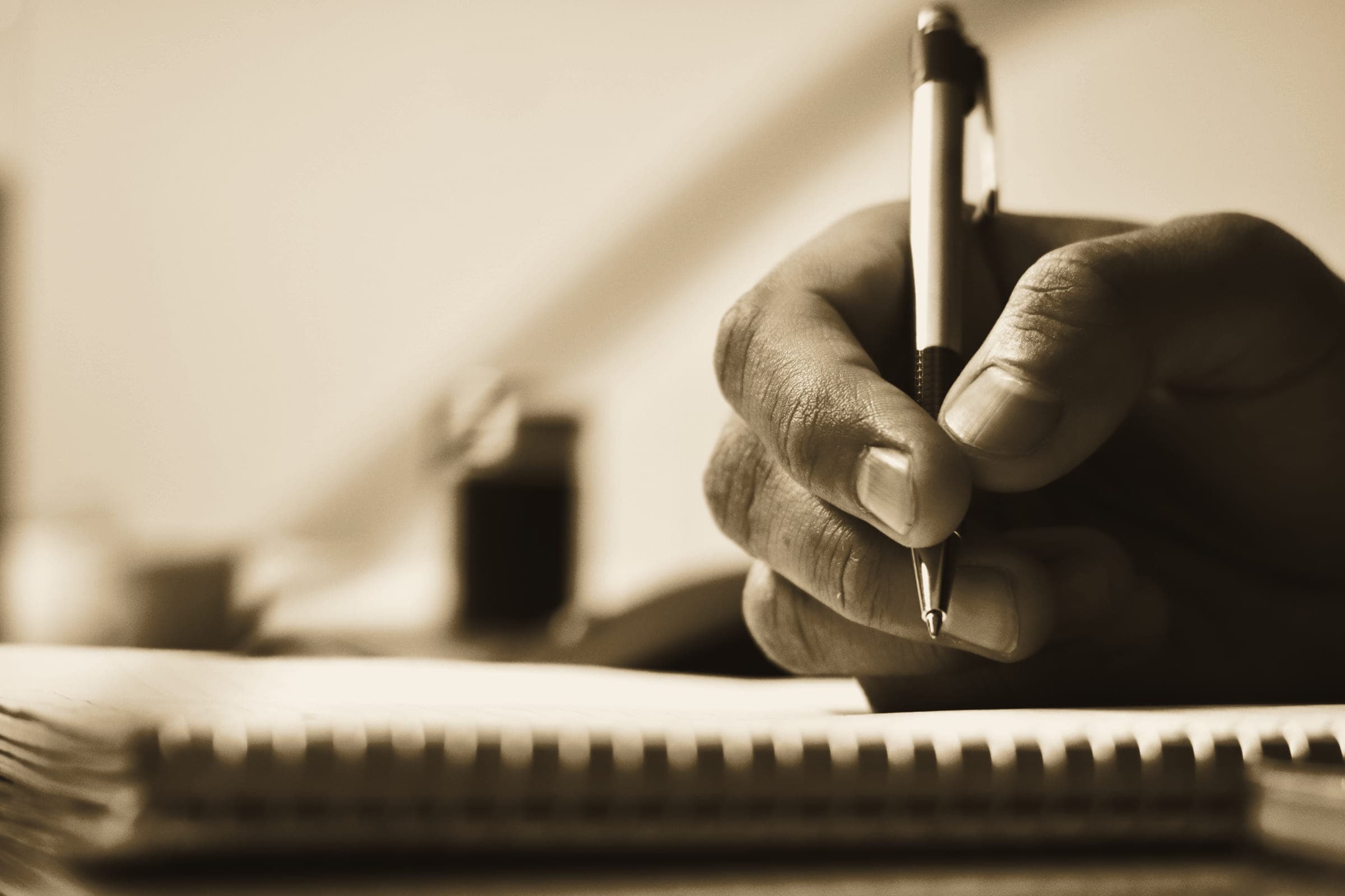 A hand writing notes in a spiral notebook with a pen, shallow focus.