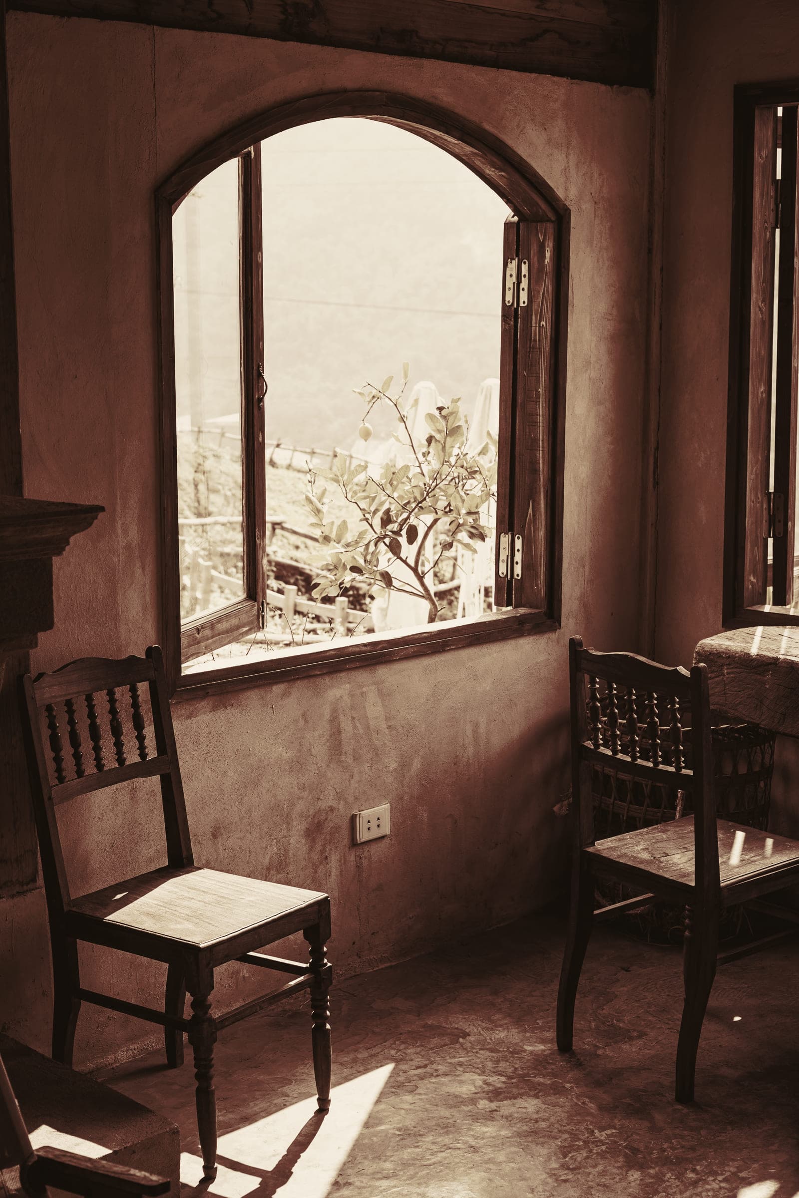 Two wooden chairs by an open arched window in warm daylight.