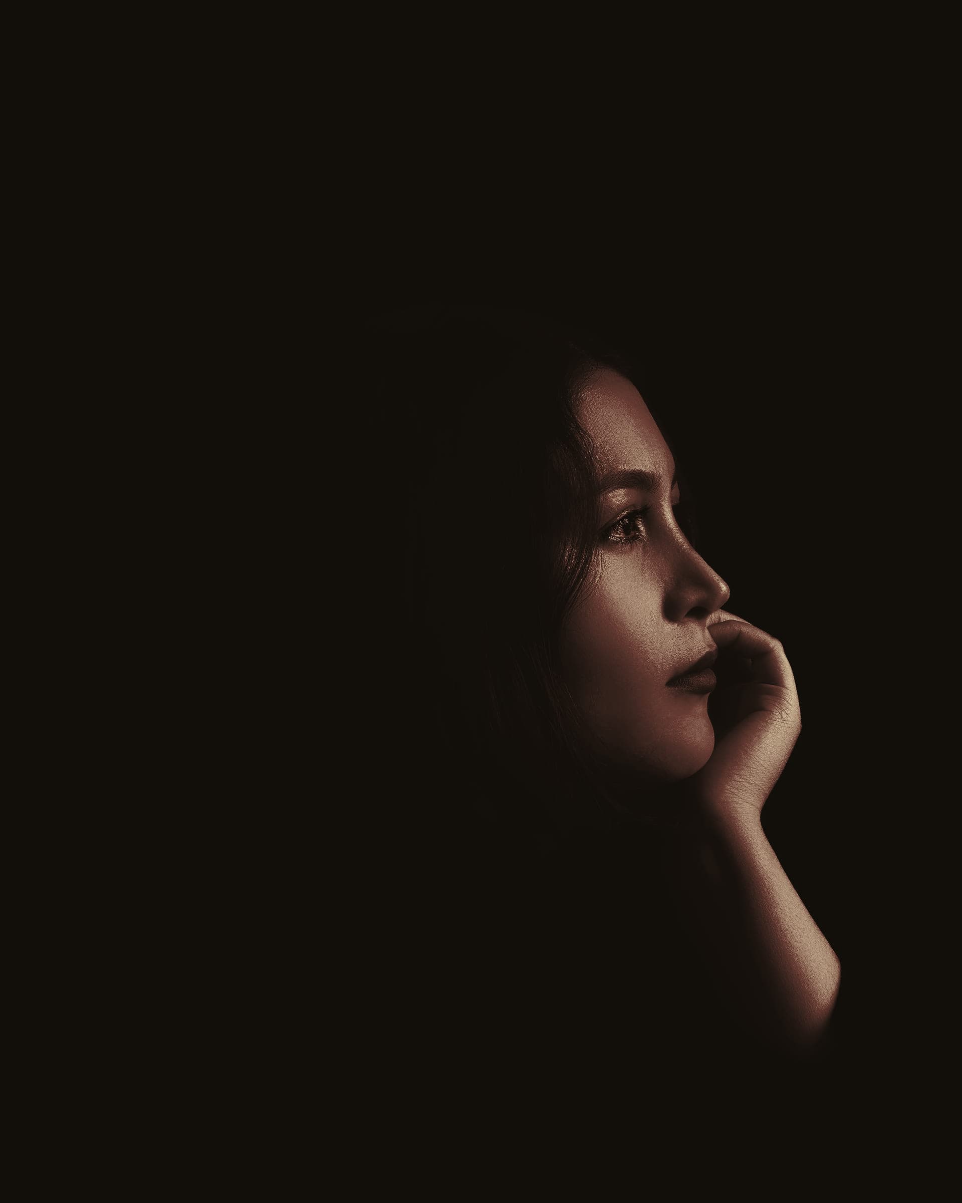 A woman in profile against a black background, her face lit by a single soft light.
